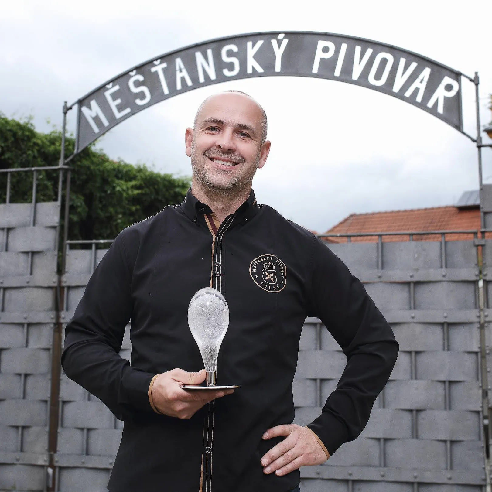 Ladislav Pártl, spolumajitel Měšťanského pivovaru Polná, stojí před bránou s nápisem Měšťasnký pivovar a drží ocenění Křišťálový špendlík.