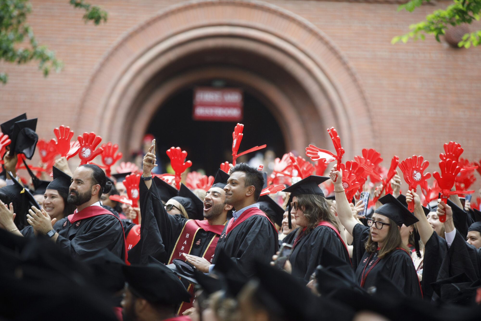 Students wearing graduation regalie celebrate with crimson clappers at Commencement.