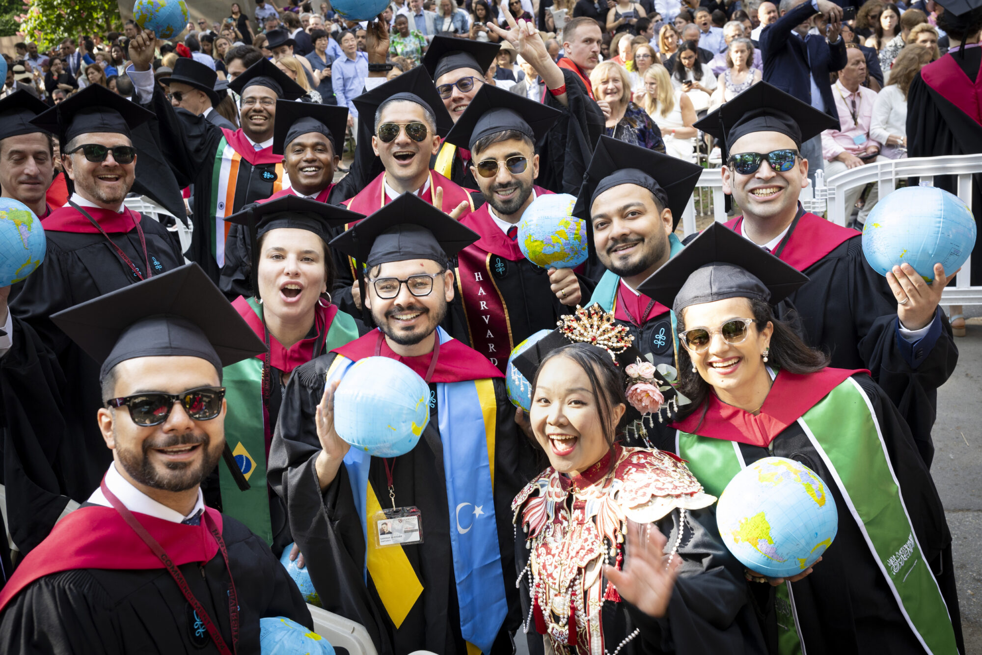 A large group of graduates from Harvard Kennedy School smile and pose holding inflatable globes