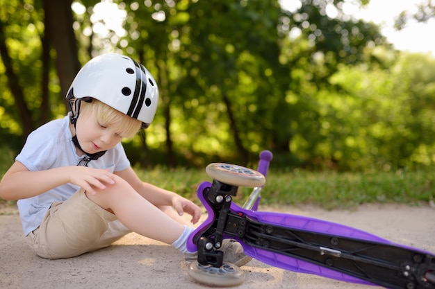 Kleinkindjunge im Schutzhelm lernend, Roller zu reiten