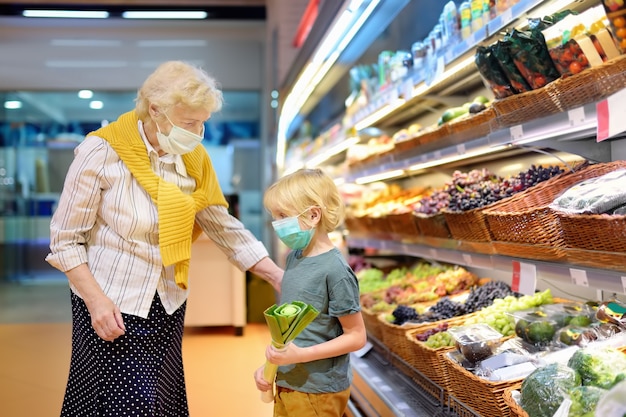Ältere Frau und ihr Enkelkind tragen medizinische Einwegmaske beim Einkaufen