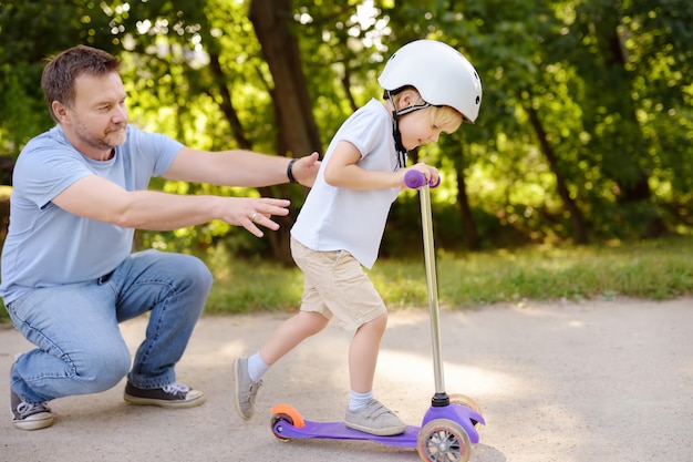 Mittelaltervater, der seinem Kleinkindsohn zeigt, wie man einen Roller in einem Sommerpark reitet