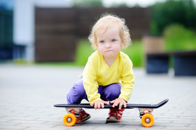 Porträt des netten Kleinkindmädchens mit Skateboard draußen