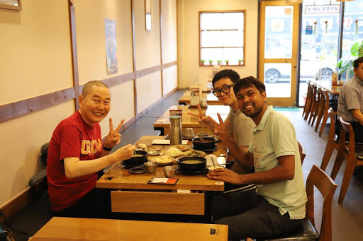 Dnyan, Kyehyun, and his father smile and throw up peace signs over a shared meal.