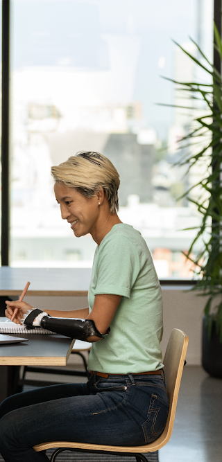 Uma mulher com braço prostético está sentada em um escritório e trabalhando no laptop.