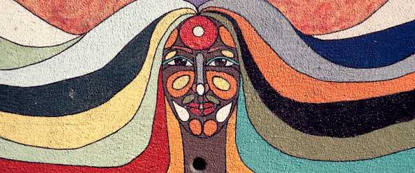 Mural on a wall of a woman's face and hair. The mural contains multiple colors on her face and hair.