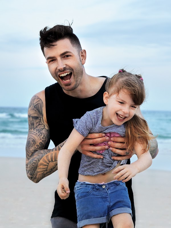 Dwayne Collins lächelt und hält seine Tochter Liberty am Strand.