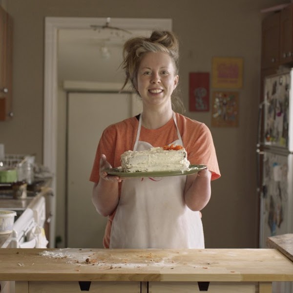 Alexis Hillyard (ella), una mujer con dismetría, de pie en una cocina y sosteniendo un pastel