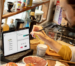 Homme dans une cuisine en désordre utilisant un stylet pour écrire une liste de courses sur sa tablette Android