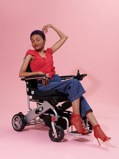 Modelo en silla de ruedas con top rojo y botas rojas frente a un fondo rosa.