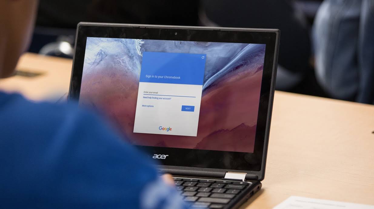 デスク上の Chromebook で Google ログイン画面を見ている生徒。