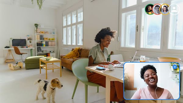 Two women are engaged in a team video call. One sits at a desk with a dog next to her. The other is smiling in the video call window.