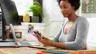 Una mujer sentada en su escritorio que mira la pantalla de un teléfono Android.
