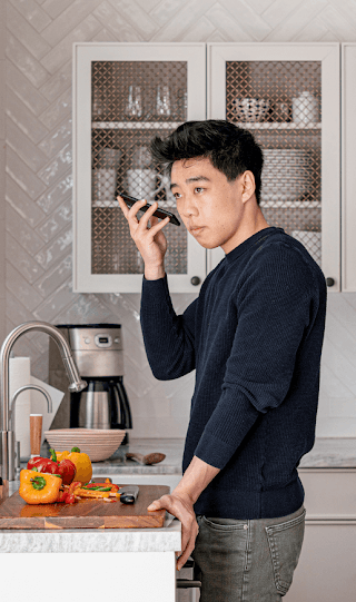 Um homem asiático-americano está no balcão da cozinha enquanto aproxima o smartphone Android do ouvido.