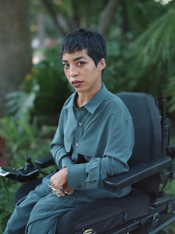 Portrait of Dominican artist and fashion model Jillian Mercado seated in a power chair facing camera