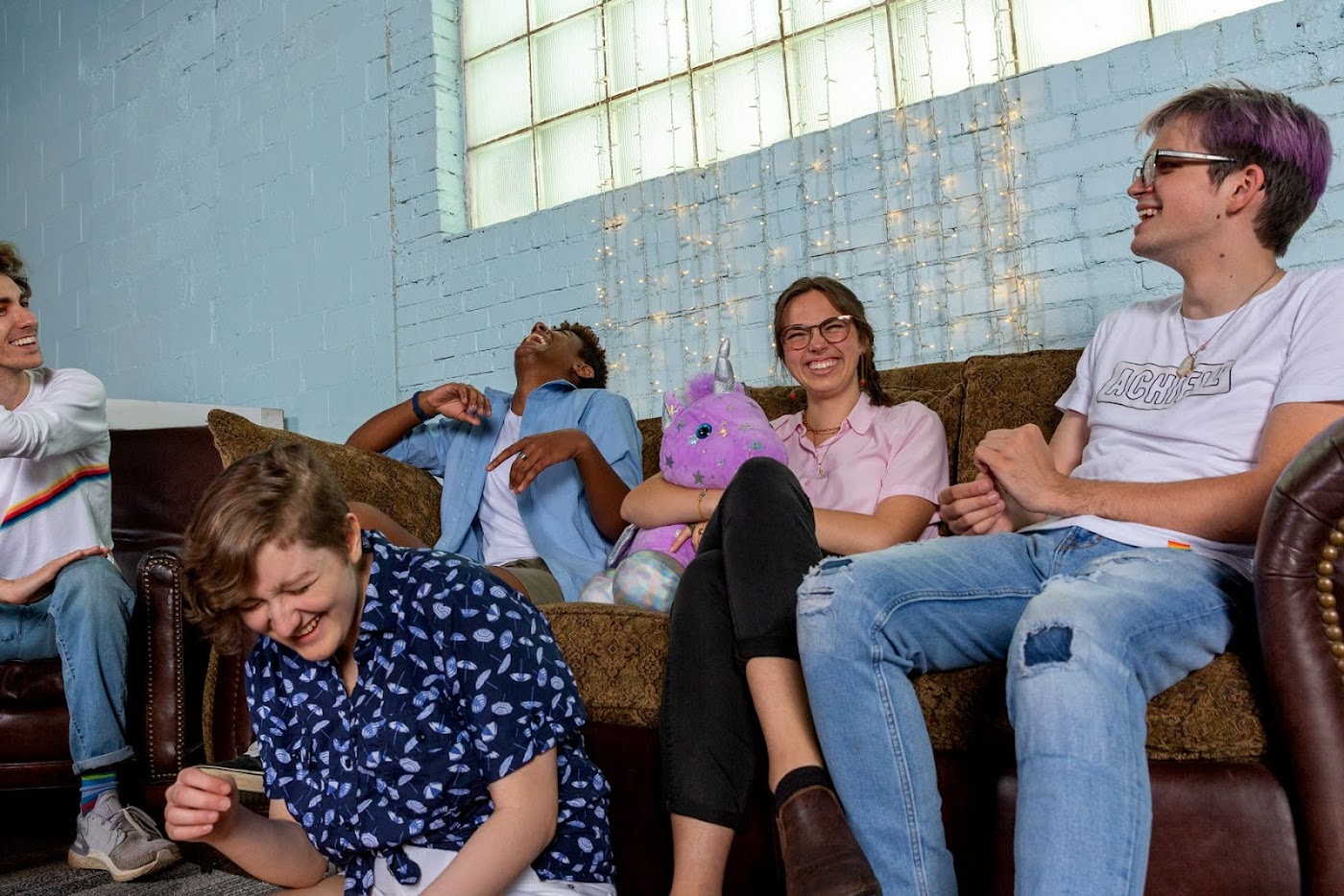 A group of younger queer people sit on a couch inside.