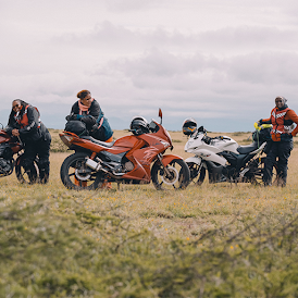 Three women in motorcycle gear stand beside each other in an open field, leaning against their motorbikes.
