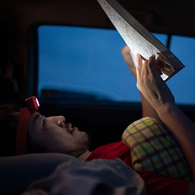 Yassan, laying in his car, checks his route on a paper map