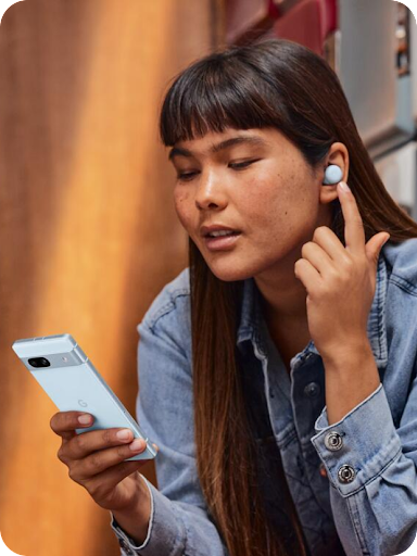 Una usuaria de Android mantiene una conversación, tocando su auricular de botón con el dedo mientras mira su teléfono Android.