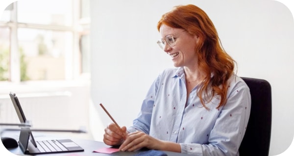Una donna che sorride e prende appunti durante una chiamata di Meet 
