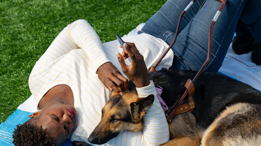 Una persona recostada sobre una manta de picnic con su perro de servicio