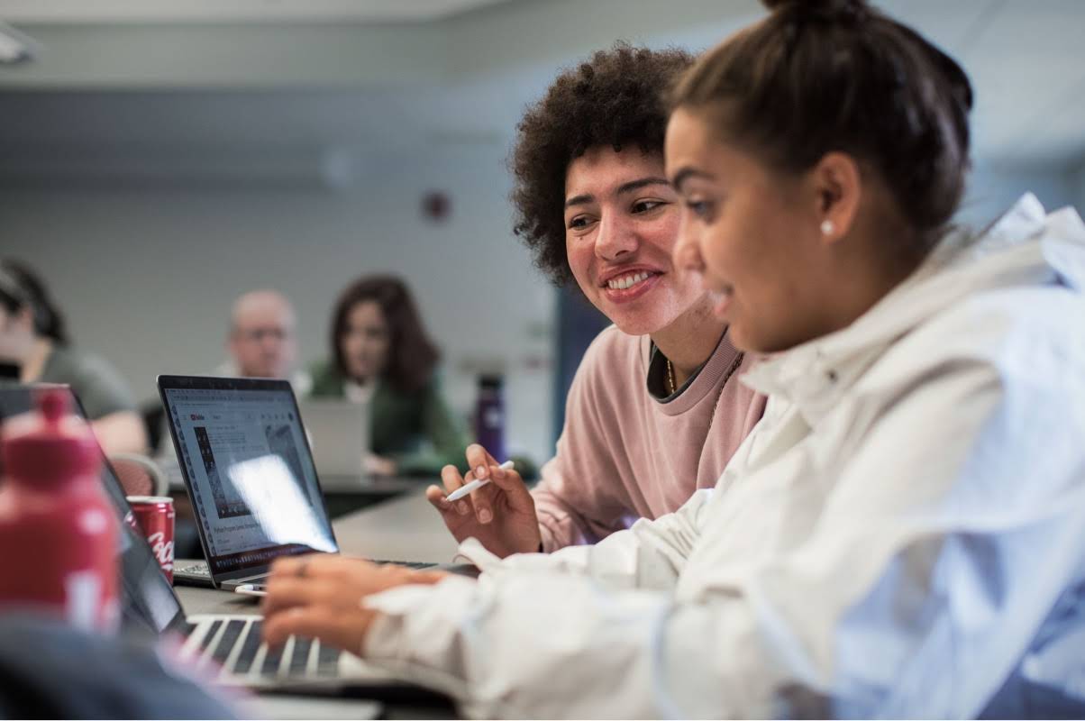 En teenager, der taster på en computer, mens en underviser giver gode råd ved hendes side