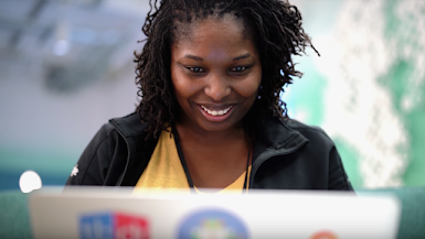 Sonriente ingeniera afrodescendiente sentada detrás de una computadora portátil