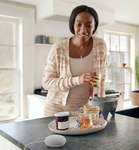 Woman drinking juice in her kitchen looking at her google home device