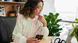 Una mujer sentada en su escritorio que sujeta un teléfono Android y mira un portátil.