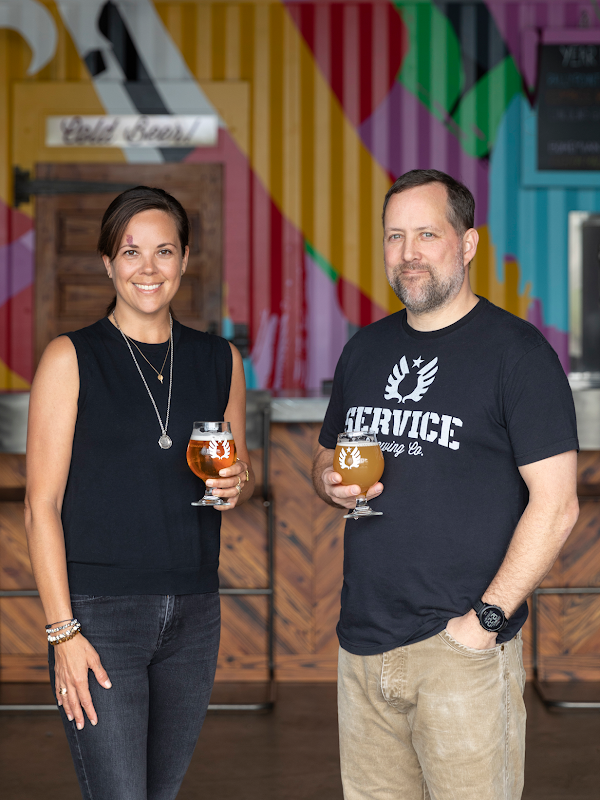 Una mujer y un hombre parados en una cervecería sostienen una copa de cerveza