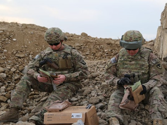 two soldiers sitting on the ground opening MREs