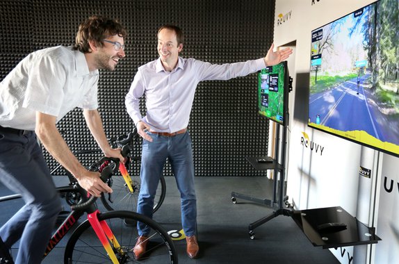 man riding a bicycle indoors in front of a screen with a video projection